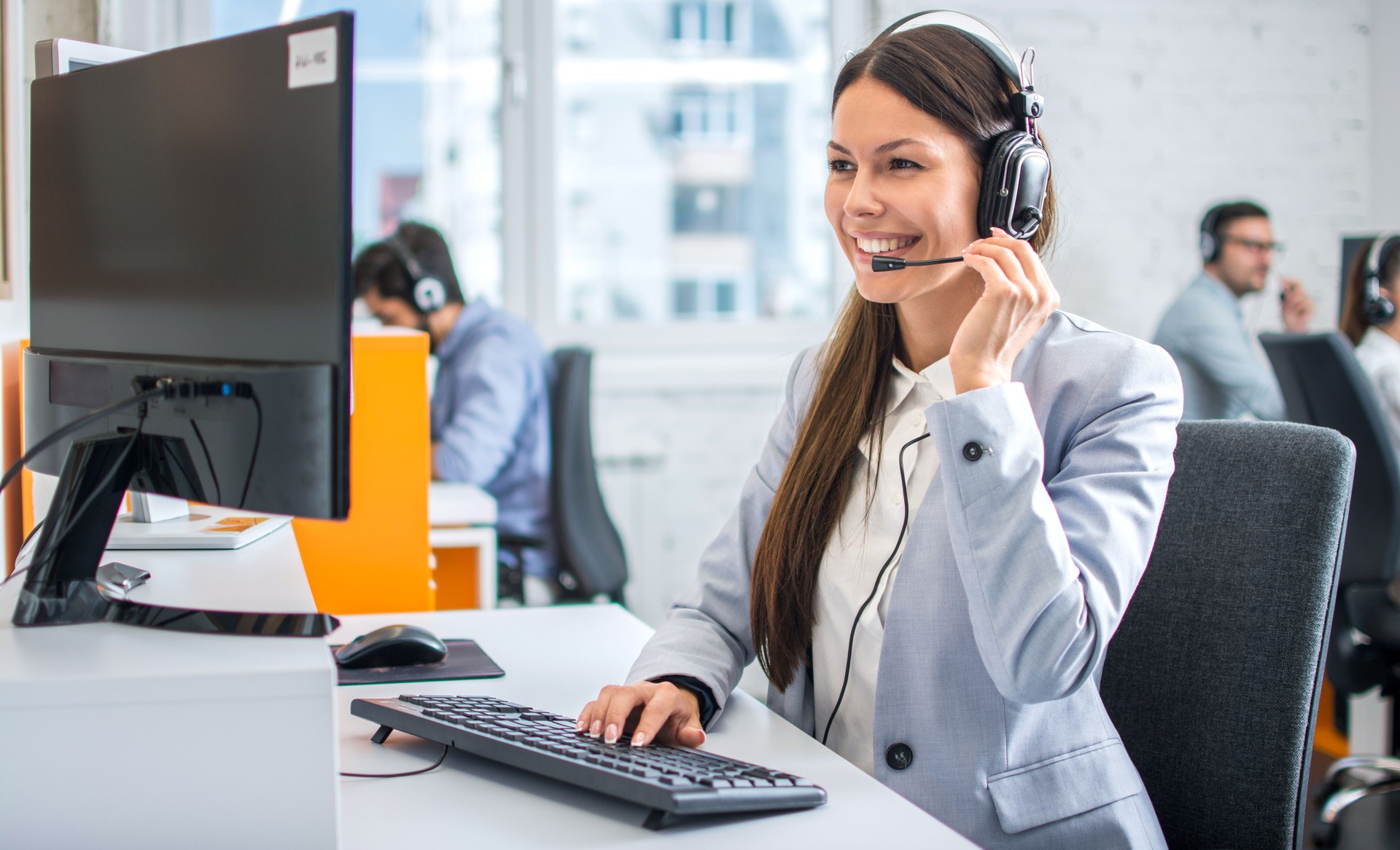 Friendly female helpline operator in call center. Young woman working in call center and holding microphone on headset with hand. Friendly female helpline operator in call center. Young woman working in call center and holding microphone on headset with hand.